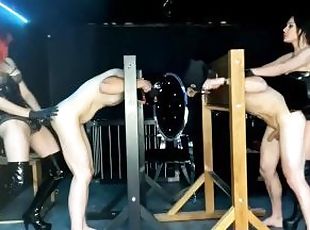 Hot Dominatrix Duo strap-on pegging their slaves in dungeon stocks